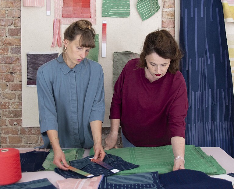Meyers_Fuegmann zwei Textildesignerinnen sehen sich bunte Stoffe auf einem Tisch an