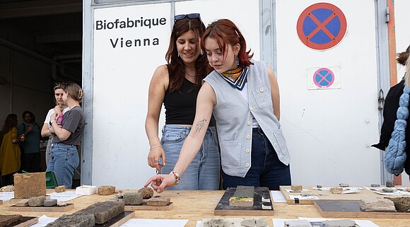 Zwei Personen sehen sich Materialien vor der Biofabrique Vienna Halle an.