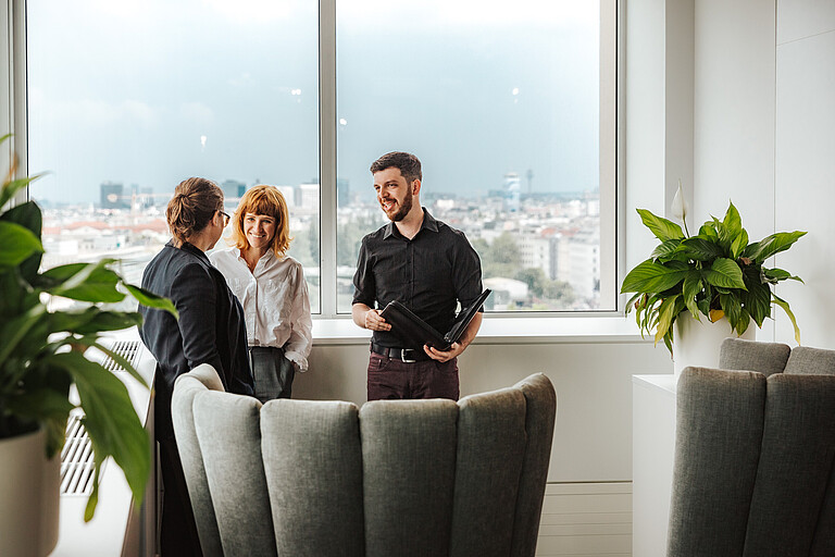 Drei Personen unterhalten sich im Stehen_Querformat Drei Personen unterhalten sich im Stehen_Querformat