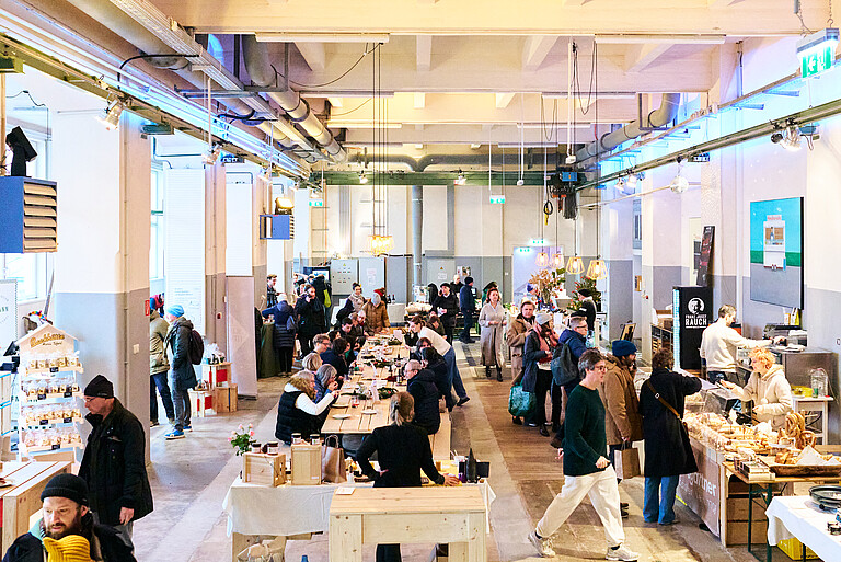 Markthalle Markterei Menschen sitzen an einem langen Tisch und manche stehen bei Verkaufsständen