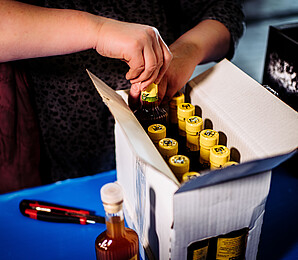 Person schlichtet Essigflaschen in eine Kartonbox