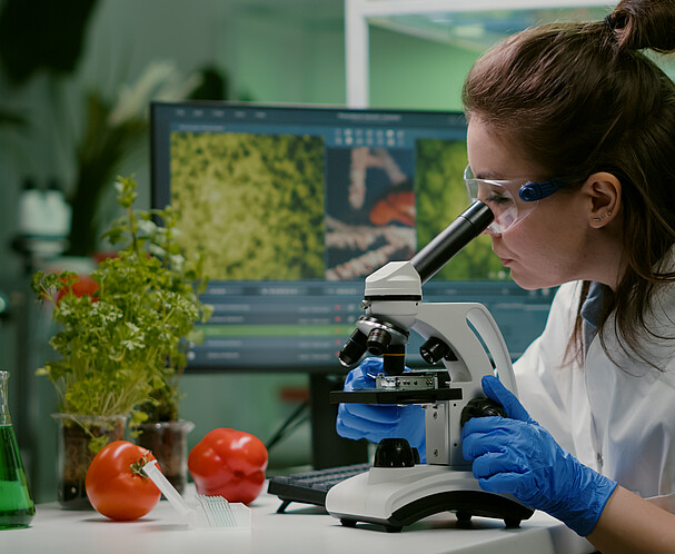 Eine Wissenschaftler*in im Labor mit Mikroskop und Lebensmitteln - Vienna Food Innovation