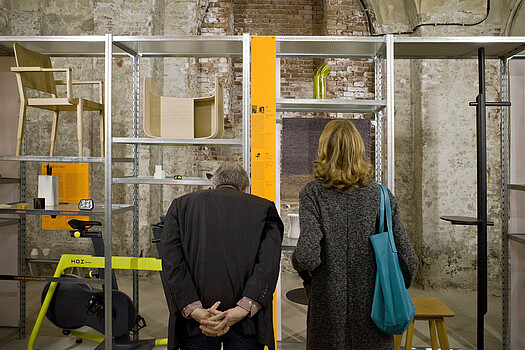 Zwei Personen betrachten auf einem Regal ausgestellte Objekte.