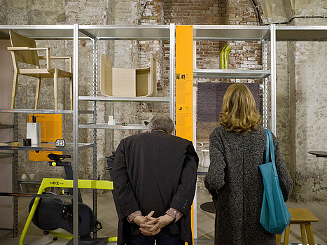 Zwei Personen betrachten auf einem Regal ausgestellte Objekte.
