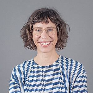 Porträt von Karin Bellmann, eine Frau mit gelockten, mittellangen Haaren und Brille