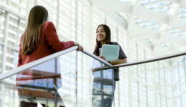 Two young women chat in a large white conference space.