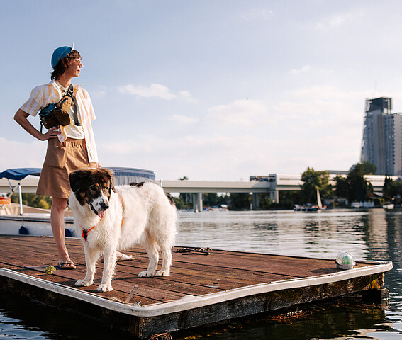 Woman with dog standing at pier and looking at tall buildings in Vienna