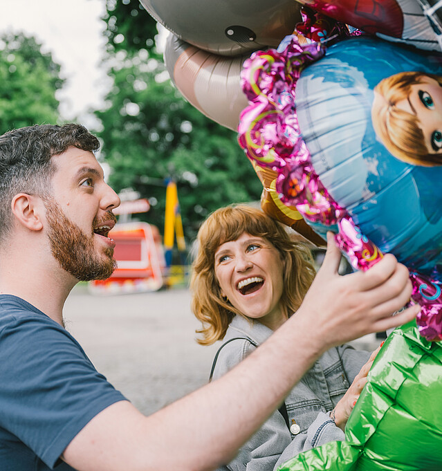 Eine Frau und ein Mann stehen lachend unter einer Traube Luftballons - Förderungen, Beratungen, Netzwerk für Unternehmen in Wien